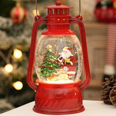 a snow globe with santa clause and christmas tree inside it on a table next to a pine cone