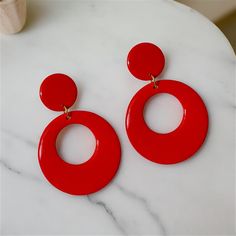 Stylish Red Dangle Hoops with a Modern Twist. Red hoop earrings in a retro style are always in vogue, having remained popular across several decades, from the 50's, 60's, 70's, 80's, and beyond. Handmade with care, these earrings are not only trendy but also enjoyable and fun to wear. Treat yourself or surprise a friend with a gift of these vibrant, medium-sized hoops made from polymer clay and coated with resin on both sides. Featuring an open circular orange hoop at the bottom connected to mat Trendy Red Circular Jewelry, Trendy Red Round Jewelry, Handmade Red Clip-on Earrings For Party, Red Clip-on Dangle Jewelry, Red Clip-on Round Jewelry, Red Round Clip-on Jewelry, Modern Red Round Earrings, Retro Dangle Clip-on Earrings For Gift, Retro Red Earrings For Gift