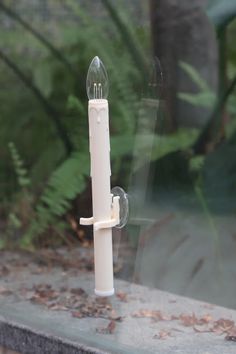 a white candle holder with two lights on it's side and leaves in the background