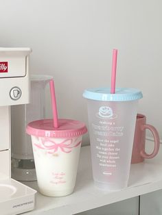 two plastic cups with straws sitting on a counter next to a coffee maker and toaster