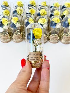 a hand holding a tiny glass bottle with flowers in it next to rows of small vases