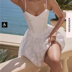 a woman in a white dress poses on a balcony overlooking the ocean and palm trees