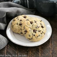 two chocolate chip cookies on a white plate next to a gray napkin and black cloth