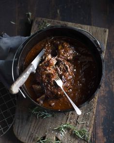 a pot filled with meat and gravy on top of a wooden cutting board