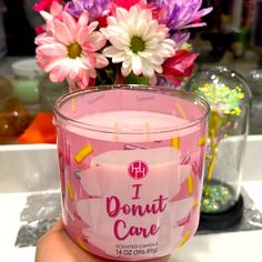 a hand holding a pink candle in front of some flowers on a table with the words i donut care written on it