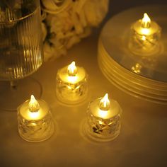 three lit candles sitting on top of a table next to plates and vase with flowers