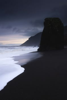 an ocean beach with waves coming in to the shore and dark clouds above, on a gloomy day