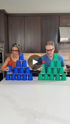 two people standing in front of a kitchen counter with cups stacked on top of each other