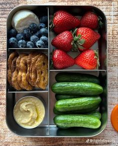 a lunch box filled with fruit, vegetables and pretzel rings on a wooden table