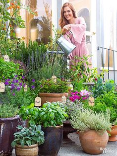 a woman is watering her garden with a watering can in front of some potted plants