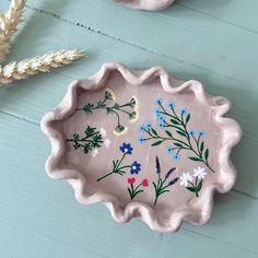 a pink bowl with flowers painted on it next to a wheat stalk and flower vase