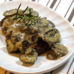 a white plate topped with mushrooms covered in gravy on top of a table