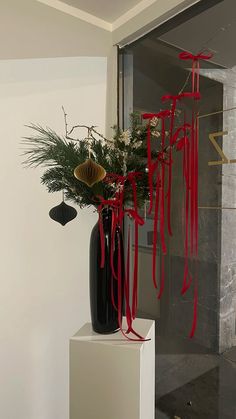 a tall black vase with red ribbons hanging from it's sides on a white pedestal