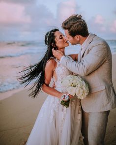 a bride and groom kissing on the beach at sunset in front of the ocean,