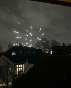 fireworks are lit up in the night sky above houses and trees on a cloudy day