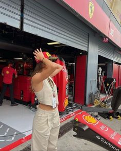 a woman standing in front of a red race car with her hand up to the side