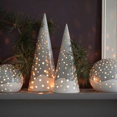 three white christmas trees sitting on top of a mantle next to pine cones with lights