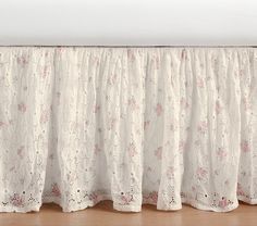 a white bed skirt with pink flowers on it and a wooden floor in the background