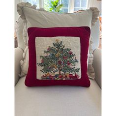 a red pillow with a christmas tree embroidered on the front and sides, sitting on a white couch