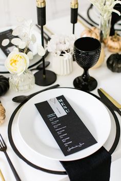 black and white table setting with place cards on the plate, silverware and candles