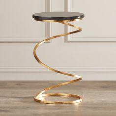 a table with a black top and gold metal spiral design on the bottom, in front of a white wall