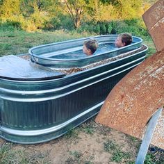 two boys are sitting in an outdoor hot tub with no cover on the side and one boy has his head above the water