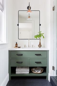 a bathroom with white walls and green drawers, black flooring and a large mirror above the sink