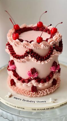 three tiered cake decorated with cherries and pink frosting on top of a plate