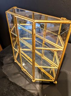 a glass case sitting on top of a table next to a black surface with gold trim