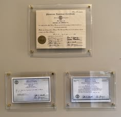 three plaques are hanging on the wall next to each other with two certificates in front of them