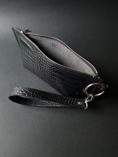 If you are a minimalist who loves carrying as little as possible but still, this black leather wristlet is the handbag you need. Compact in size and elegant in shape, this crocodile print leather handbag accommodates your basics. It will keep your phone, money, and something tiny perfectly protected by a metal zipper. A durable lining adds an extra touch, making this bag finite and super attractive.  A sturdy, two-layer wrist band, featuring a delicate clasp hook, will adjust to your moves over Black Pouch With Wrist Strap For Daily Use, Handheld Clutch With Wrist Strap For Everyday Use, Everyday Handheld Clutch With Wrist Strap, Black Clutch With Wrist Strap Gift, Modern Rectangular Clutch With Wrist Strap, Formal Rectangular Bag With Wrist Strap, Leather Handheld Bag With Wrist Strap, Handheld Leather Bag With Wrist Strap, Modern Clutch With Wrist Strap For Daily Use