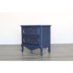 a blue nightstand with two drawers and gold trimmings on the top, against a white wall