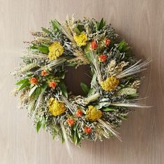 a wreath with yellow flowers and green leaves on a wooden surface in front of a wall