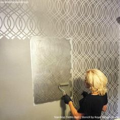 a woman is painting a wall with white paint and silver stencils on it