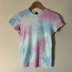 a pink and blue tie dye shirt hanging on a hanger against a white wall