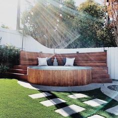 a wooden hot tub sitting in the middle of a lush green yard next to a white fence