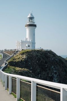 a white lighthouse on top of a hill next to the ocean with a fence around it