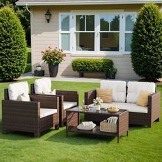 an outdoor living area with wicker furniture and potted plants on the grass in front of a house