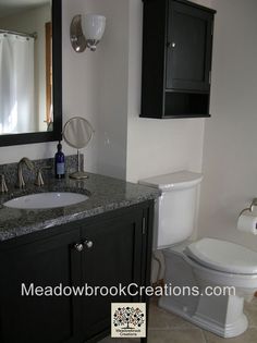 a white toilet sitting next to a sink in a bathroom under a mirror and cabinet