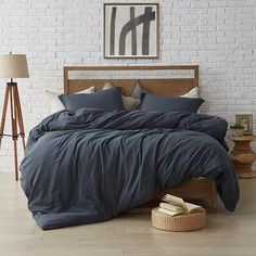 a bed with blue sheets and pillows in a white brick room next to a lamp