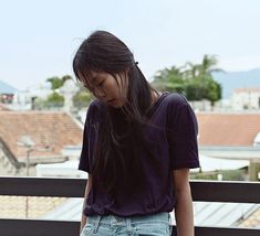 a young woman standing on top of a balcony next to a railing looking down at her cell phone