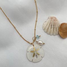 Legend has it that finding a sand dollar during a beach stroll is considered a lucky omen. So take a little bit of the beach and good luck with you wherever you go with our gorgeous Sand Dollar Charm Necklace. Features our most loved satellite chain, freshwater pearl, and blue zircon accents. Freshwater Baroque Pearl size: 6 to 8mm Blue Zircon roundel gemstone 4mm 14kt gold fill or sterling silver round beads 2mm 14kt gold fill or sterling silver satellite chain Real sand dollars are preserved a Cheap Beach Pendant Jewelry, Cheap White Charm Necklaces For The Beach, Unique Cheap Beach Jewelry, Cheap Trendy Beach Jewelry, Chic Affordable Beach Jewelry, Cheap Pearl Charm Necklace For Beach, Cheap Beachy Jewelry For Beach Season, Sand Dollar Jewelry, Sand Dollar Necklace