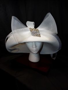 White Prairie Derby Hat with Bow and Rhinestone Accents Make a statement with this exquisite white derby hat. Featuring a wide brim, a flowing bow, and a sparkling rhinestone embellishment, this hat is perfect for adding a touch of elegance to any formal occasion. Wide, elegant brim Flowing bow Sparkling rhinestone embellishment High-quality material Timeless design Ideal for weddings, church services, and special events Make a Statement Today! Elevate your style with this unique accessory--shop now and turn heads at your next event! Elegant White Rhinestone Headpieces, White Fitted High Crown Hat, Elegant White Hat With Rhinestones, Formal Rhinestone Hats For Kentucky Derby, Rhinestone Party Hat For Kentucky Derby, White Fitted Hat With Pinched Crown, Elegant High Crown Top Hat For Party, Elegant Evening Hats With Rhinestones, White Adjustable Hats With Structured Crown