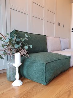 a green couch sitting on top of a hard wood floor next to a vase filled with flowers