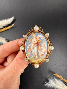 Antique Venus & Cupid Brooch 14ct Gold Stamped  Circa 1860s Introducing an exquisite early Victorian 14ct gold stamped cherub portrait brooch, featuring a beautifully hand-painted enamel portrait depicting Venus & Cupid in a happy, vibrant outdoor scene. The enamel is encased in a fabulous ornate frame decorated with diamonds and pearls, adding an extra touch of elegance and sophistication. This versatile brooch can also be converted into a pendant upon request, allowing for multiple styling opt Vintage Yellow Gold Baroque Brooch, Victorian Yellow Gold Collectible Brooch, Antique Baroque Brooches With 17 Jewels, Yellow Gold Baroque Brooches As Gift, Baroque Yellow Gold Brooch For Gift, Yellow Gold Baroque Brooch For Gift, Victorian Baroque Brooches As Gifts, Heirloom Cameo Brooch Gift, Heirloom Cameo Brooches As Gift