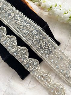 two white beaded trims on black velvet with flowers in the backgroud