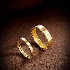 two gold wedding rings sitting next to each other on a brown surface with dark background