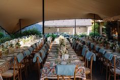 an outdoor dining area with tables and chairs covered in blue linens, surrounded by greenery