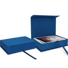 an open blue box sitting on top of a white table next to a book and ribbon