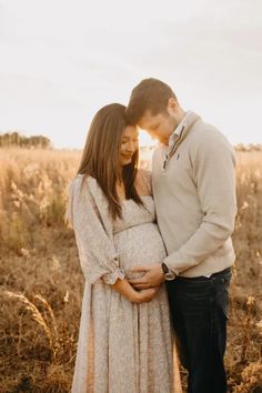 a pregnant couple cuddles in the middle of an open field at sunset during their newborn photo session